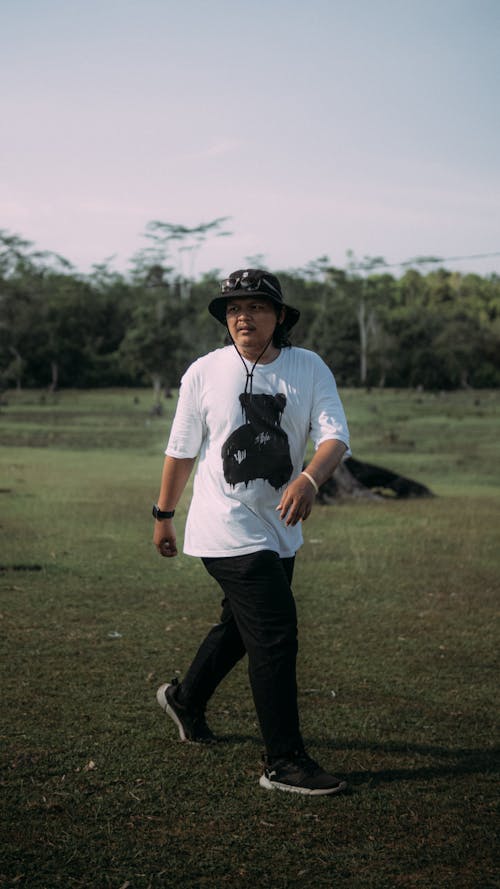 A man in a black t - shirt and hat walking through a field