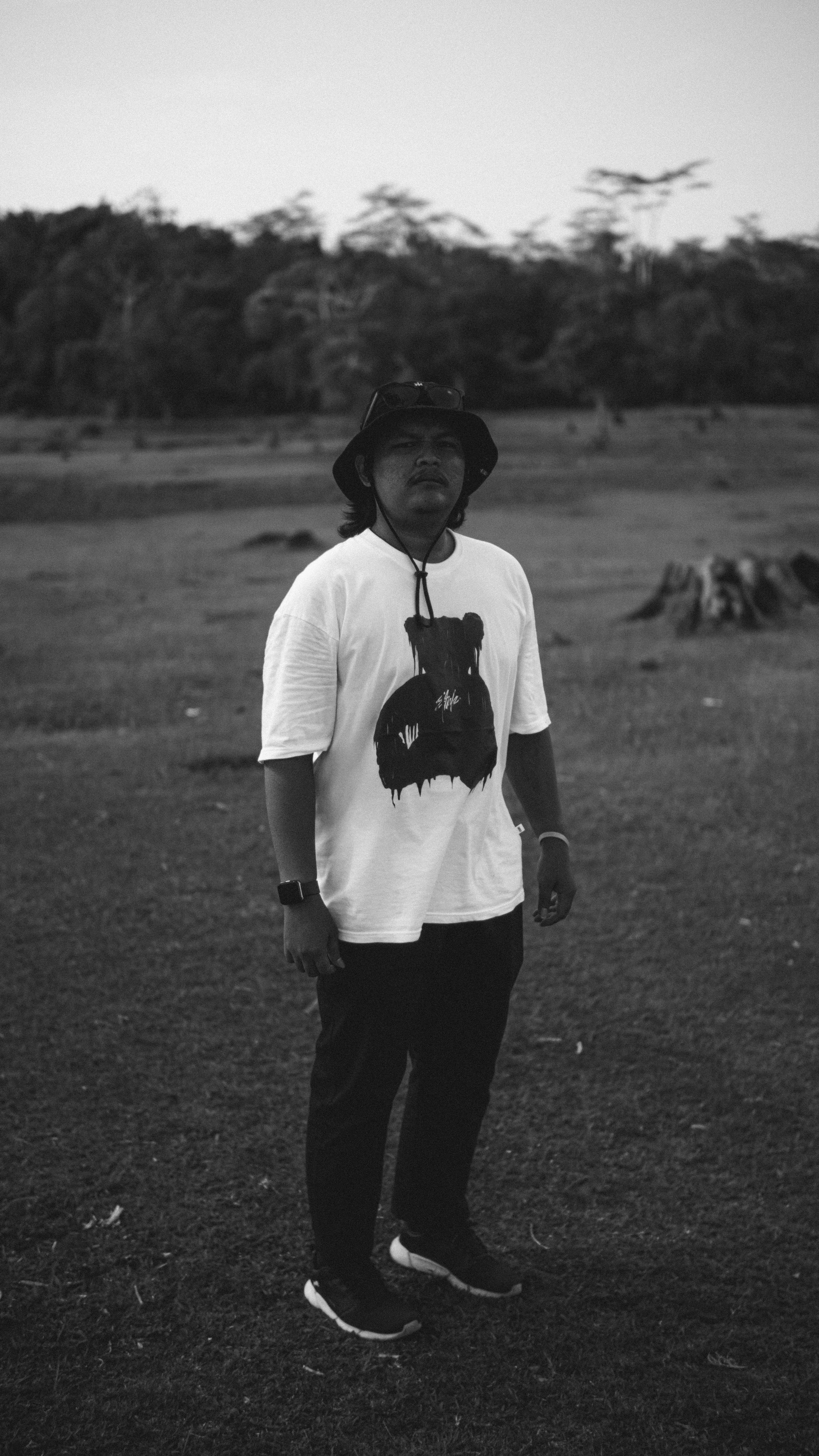 Black and white portrait of a man wearing casual attire, standing in a field.