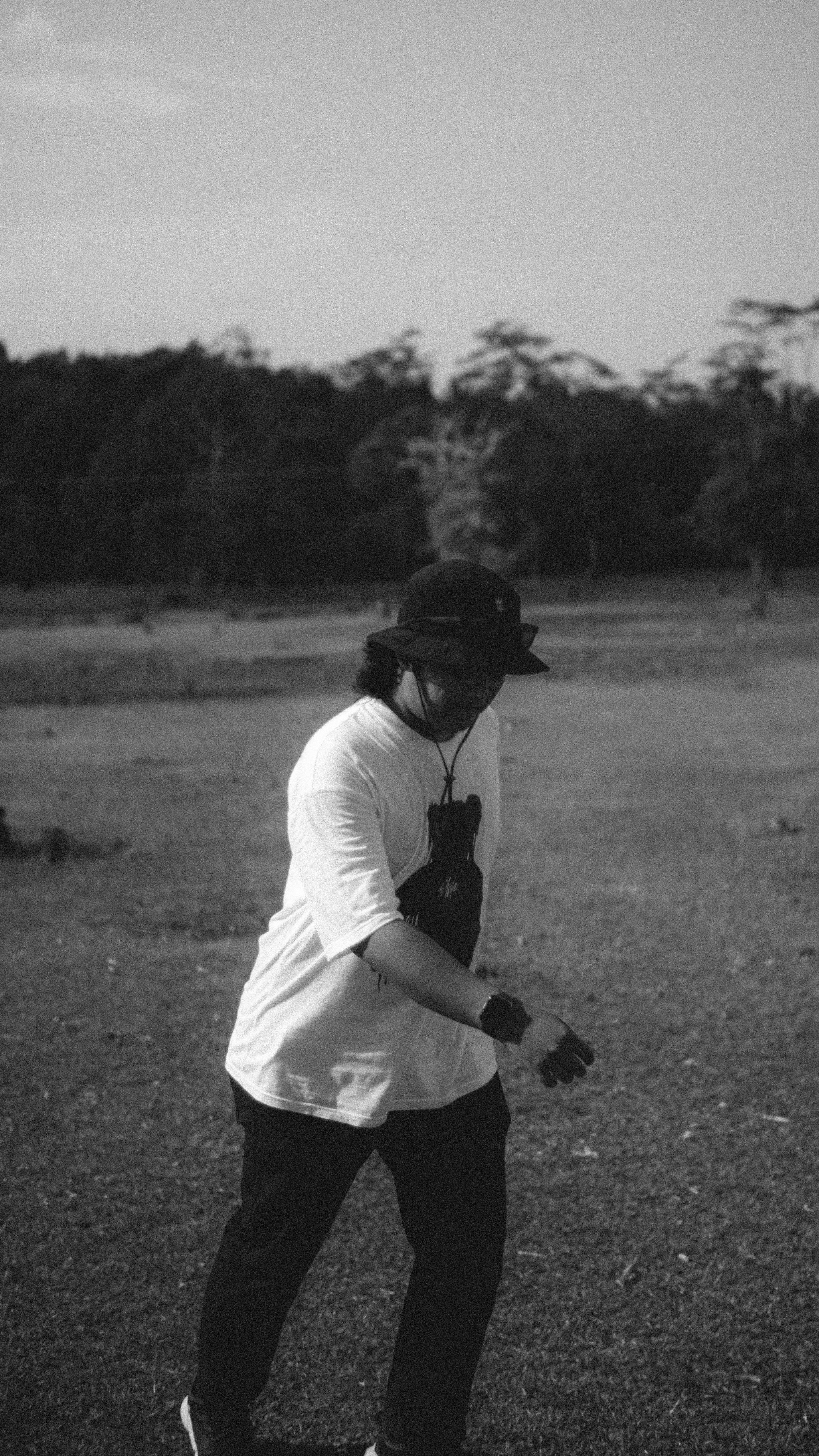 Black and white photo of a man walking in a rural field, wearing a hat.