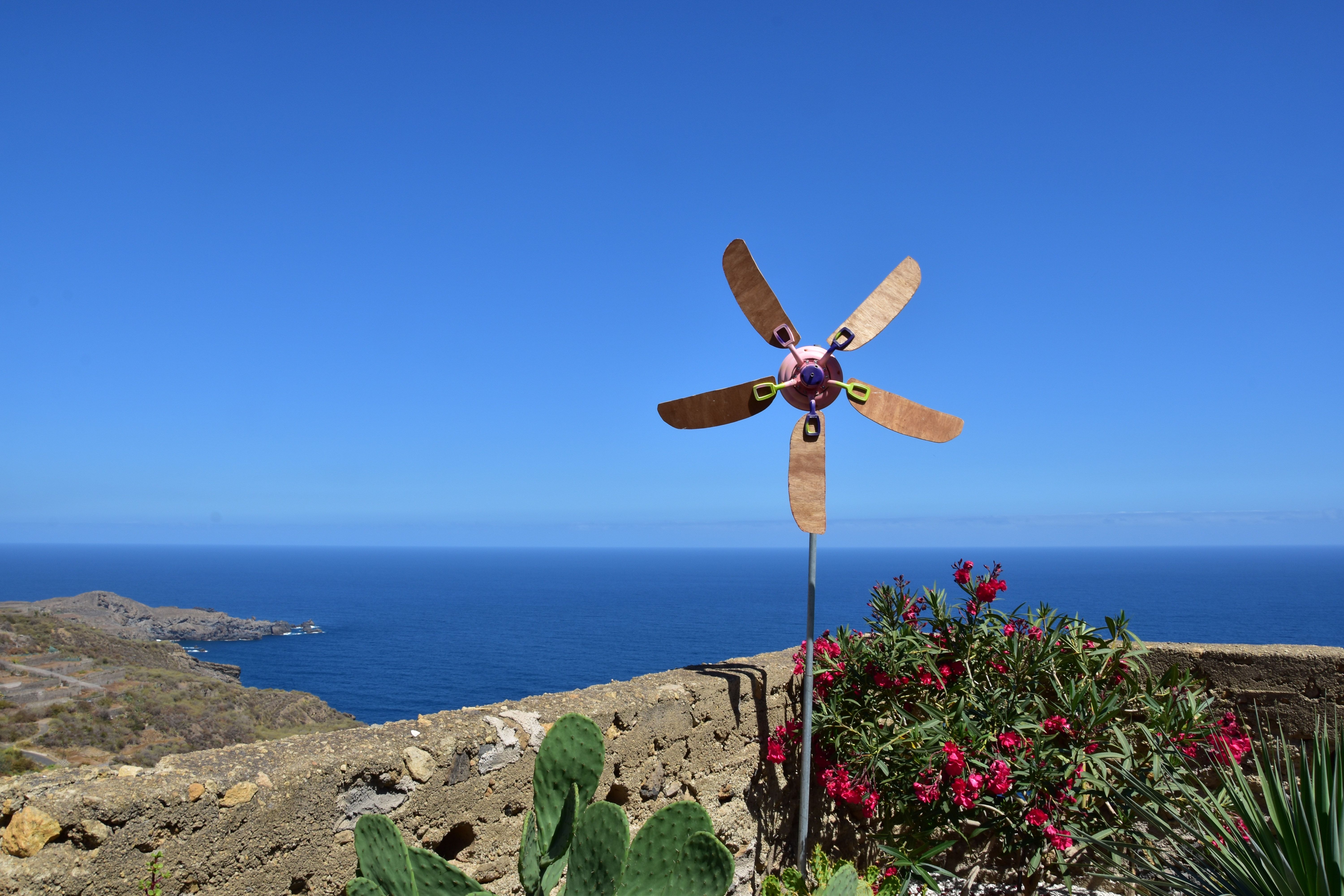 Vibrant windmill overlooking the sea, surrounded by lush flora on a bright summer day.