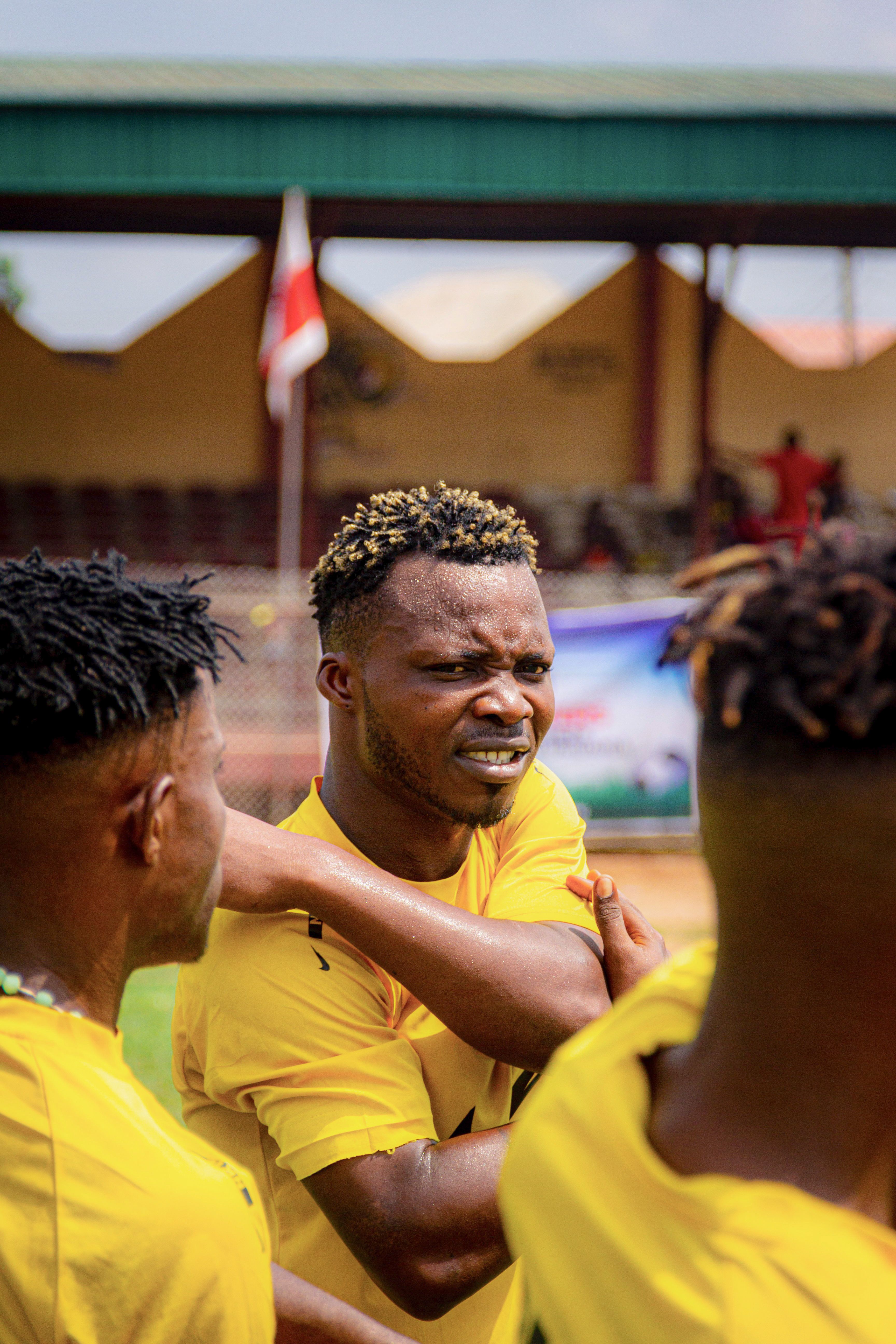 African soccer players in yellow jerseys stretch before a match on an outdoor field.