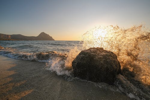 A rock splashing into the ocean at sunset