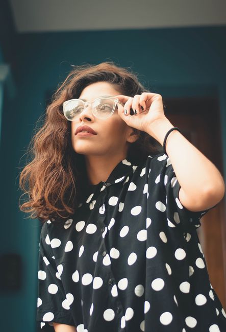 Stylish woman adjusts sunglasses while wearing a polka dot dress, exuding elegance and modern fashion.
