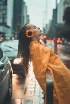 一名穿着黄色雨衣的妇女，倚靠在城市灯光映照下潮湿的街道旁