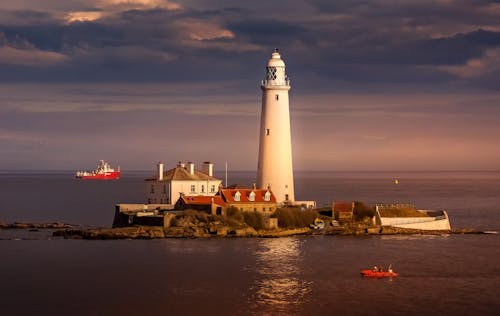 A lighthouse is sitting on a rocky shore with boats in the water