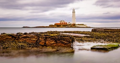 Free Scenic view of St Mary's Lighthouse in Whitley Bay with rocky foreground and cloudy sky. Stock Photo