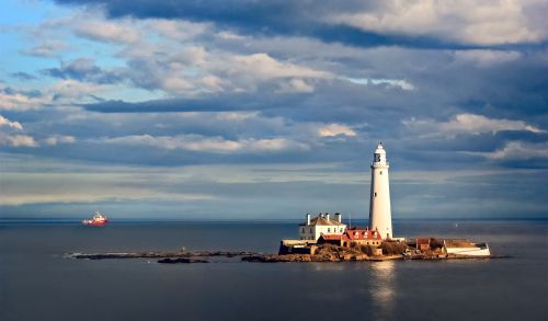 Free Picturesque view of St. Mary's Lighthouse and distant ship under a dramatic sky, perfect for travel enthusiasts. Stock Photo