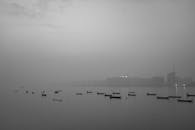 这张宁静的黑白照片拍摄了薄雾水域中的船只，背景是城市天际线