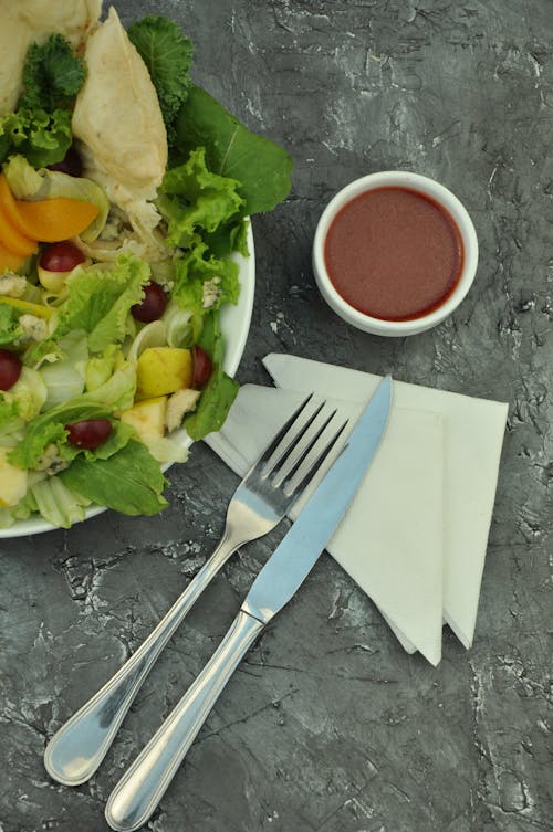 бесплатная Серебряная вилка и хлебный нож возле овощного салата на тарелке Стоковое фото