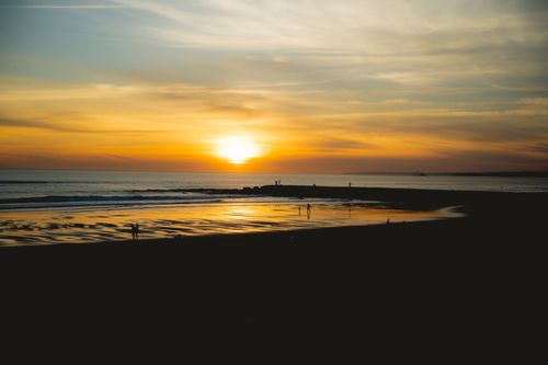 Free Silhouetted figures against a vibrant beach sunset, perfect for tranquil themes. Stock Photo