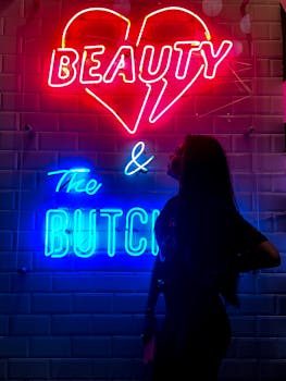 在黑暗的环境中，一名女子站在霓虹灯标志的映衬下，上面写着“美女与布奇”，灯光充满活力