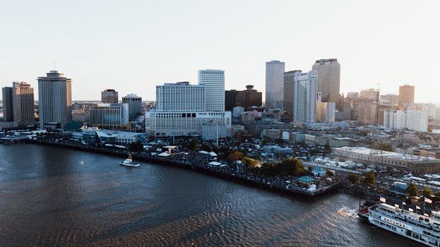 Drone shot capturing the bustling cityscape of New Orleans and the Mississippi River at dusk.