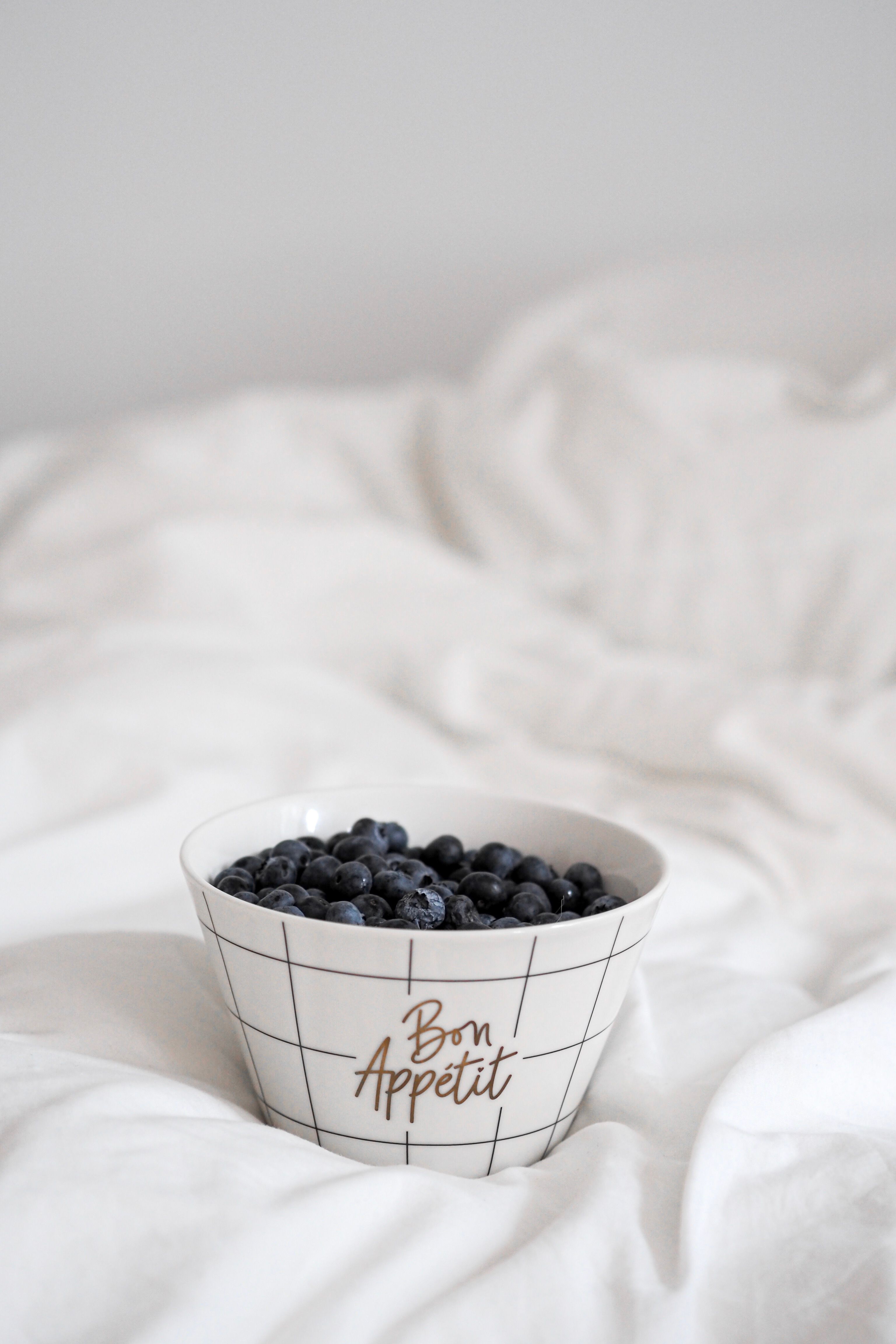 A bowl of fresh blueberries on a white bed with elegant 'Bon Appétit' text.