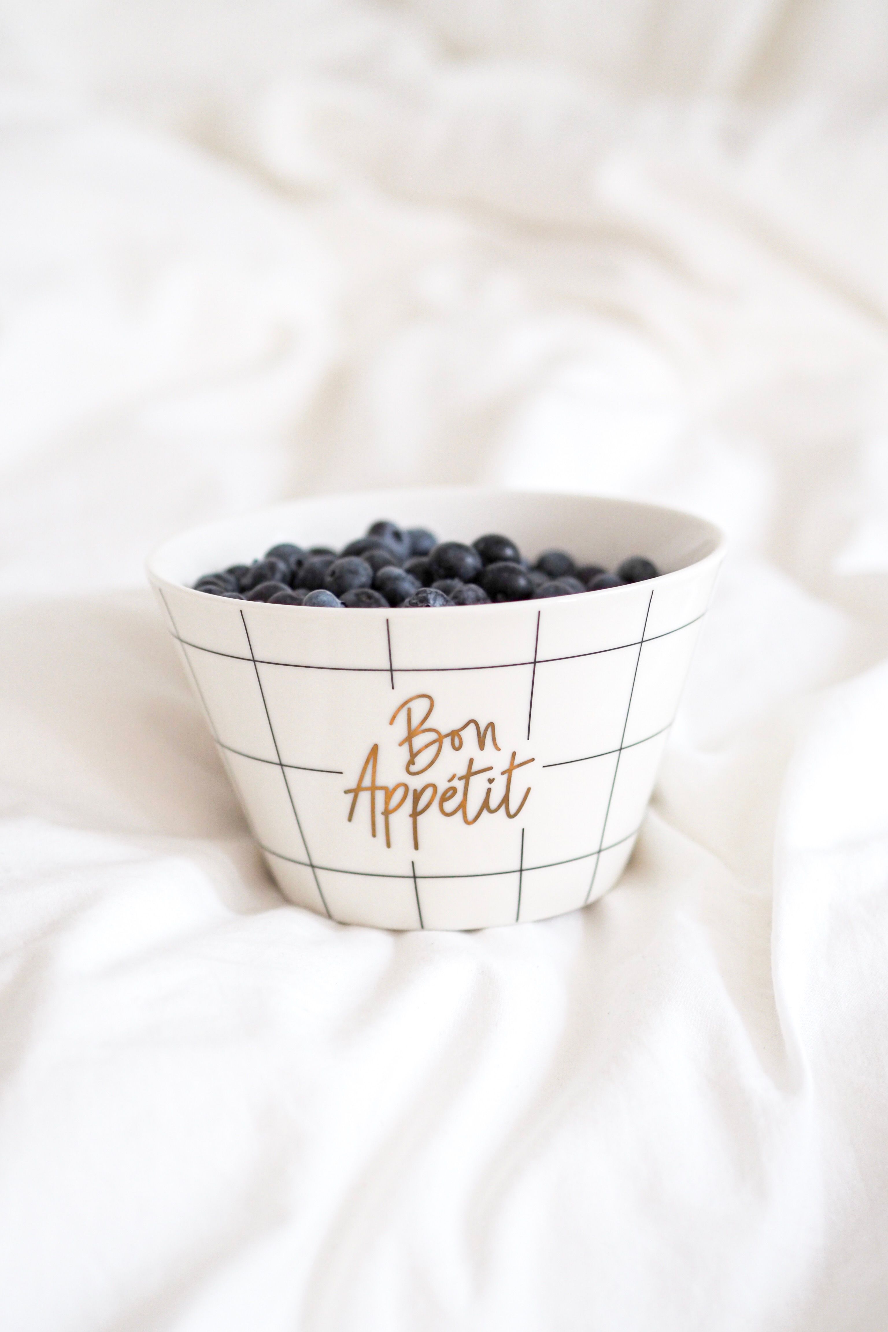 A bowl of blueberries on a white linen, featuring 'Bon Appetit' text in Parisian style.