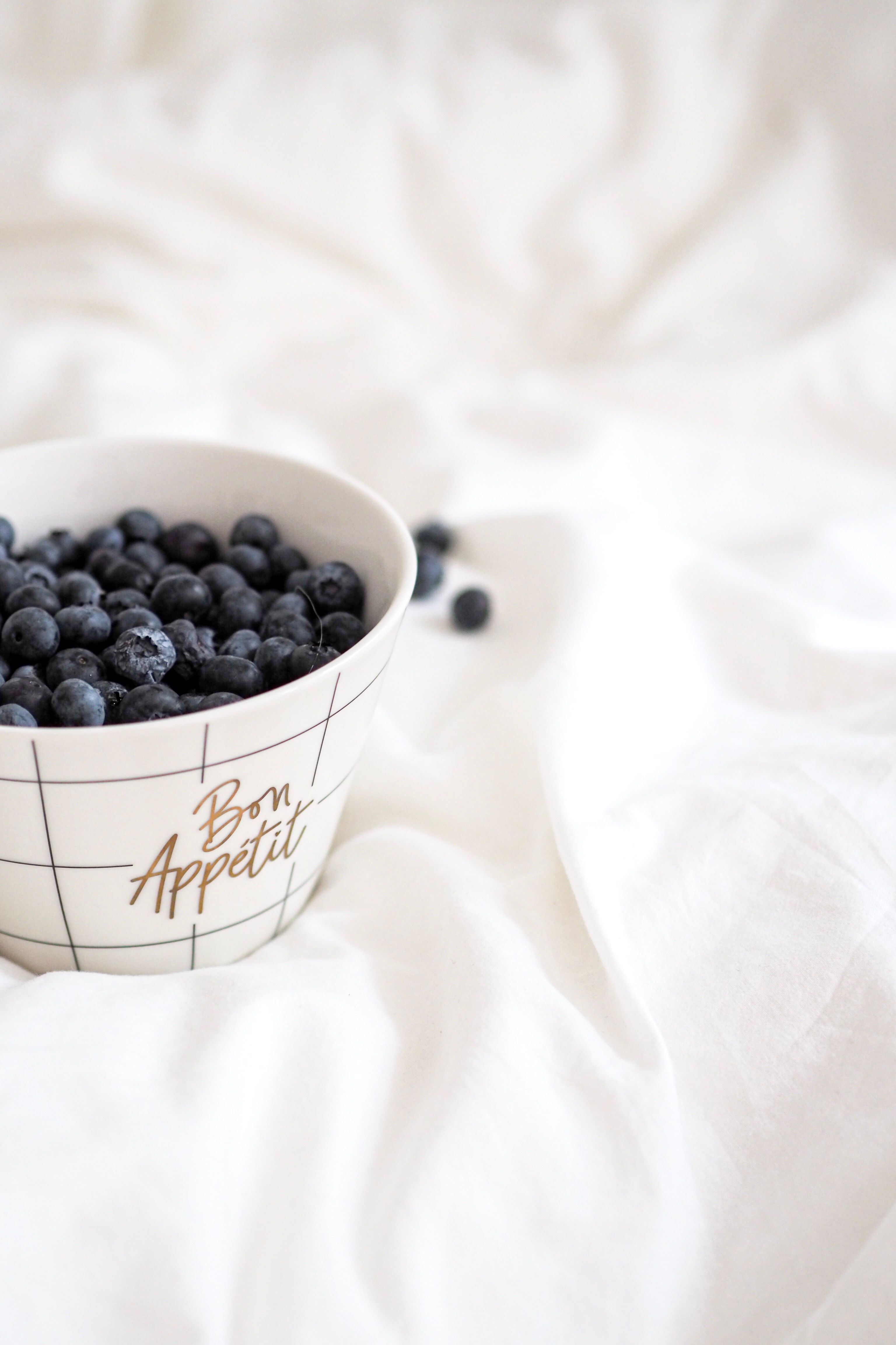High angle view of fresh blueberries in a Bon Appétit bowl on white fabric, emphasizing healthy eating.