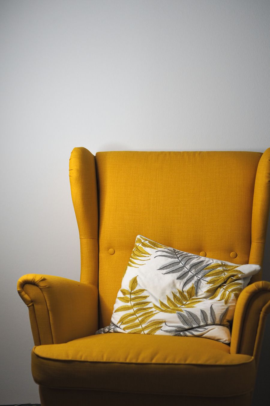 Mustard wing armchair with a patterned cushion — photo by Laura Chouette on Pexels