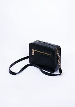 Stylish black leather bag with gold accents against a white background in a minimalist studio shot.