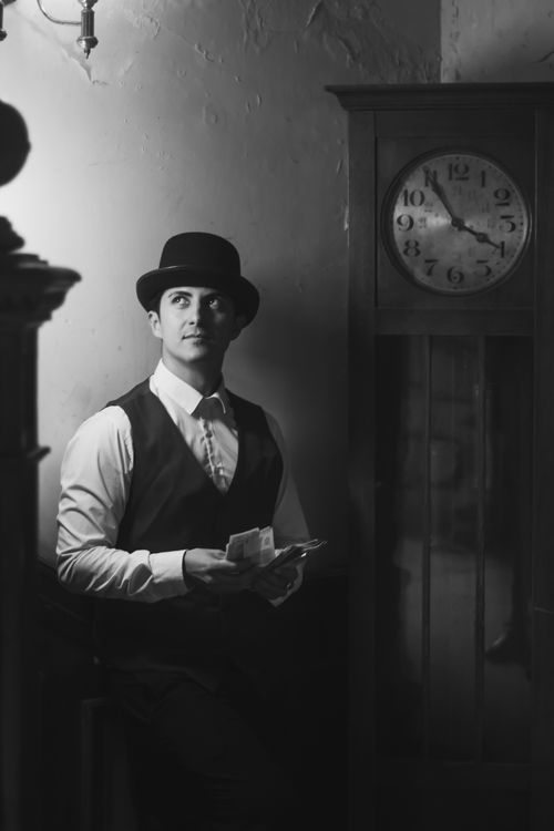 Free Black and white portrait of a man in a bowler hat standing beside an antique clock, evoking a vintage feel. Stock Photo