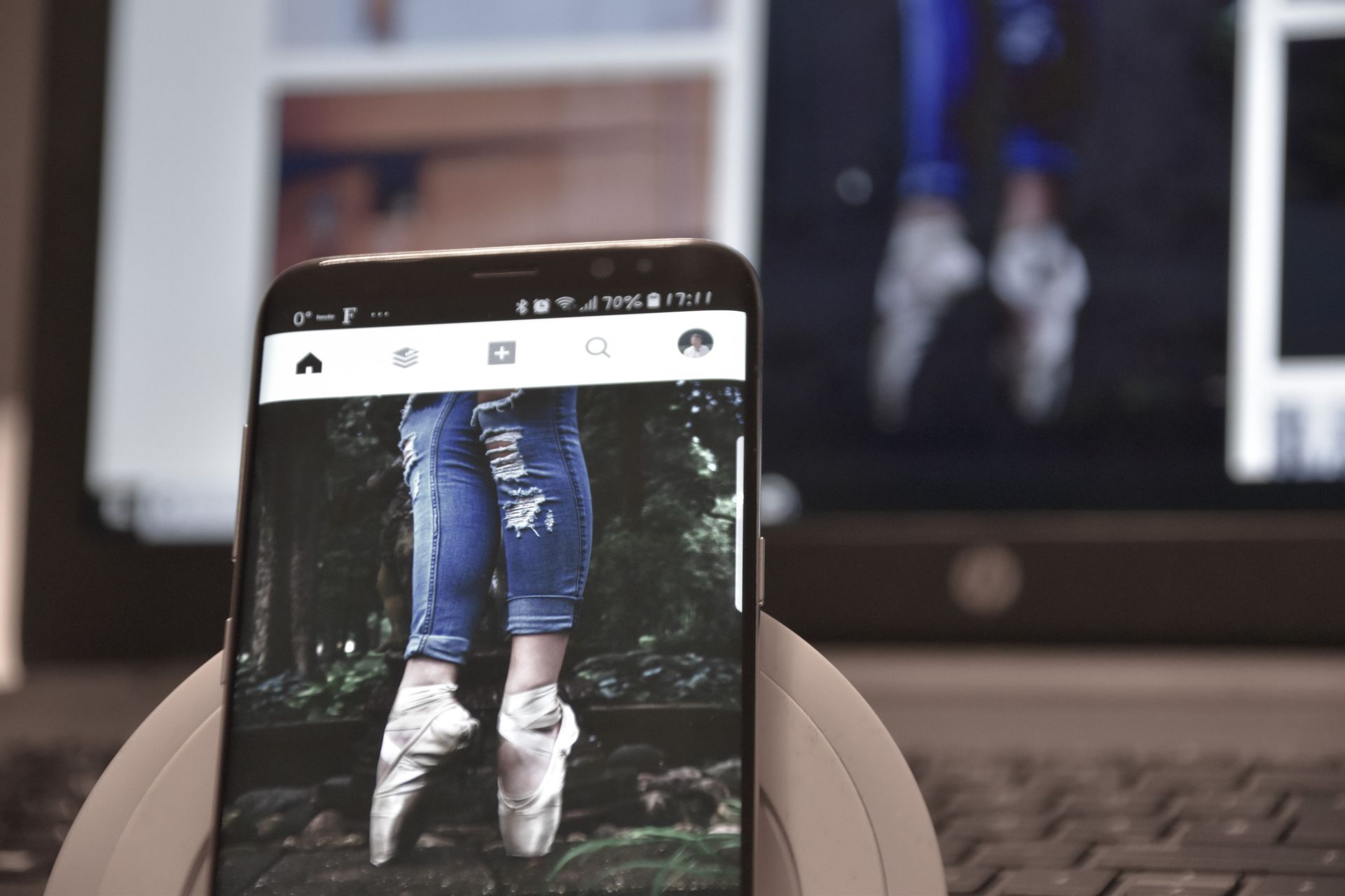 A ballet dancer in pointe shoes displayed on a smartphone in front of a laptop screen indoors.