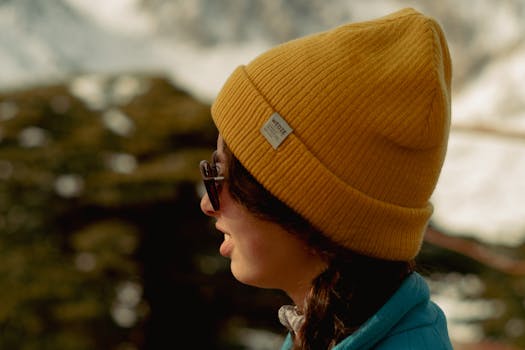 Outdoor portrait of woman wearing a yellow beanie and sunglasses, enjoying a scenic view.