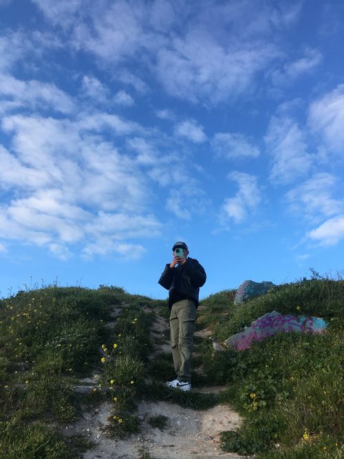 Free A person stands on a rural pathway capturing photos with a smartphone under a bright blue sky. Stock Photo
