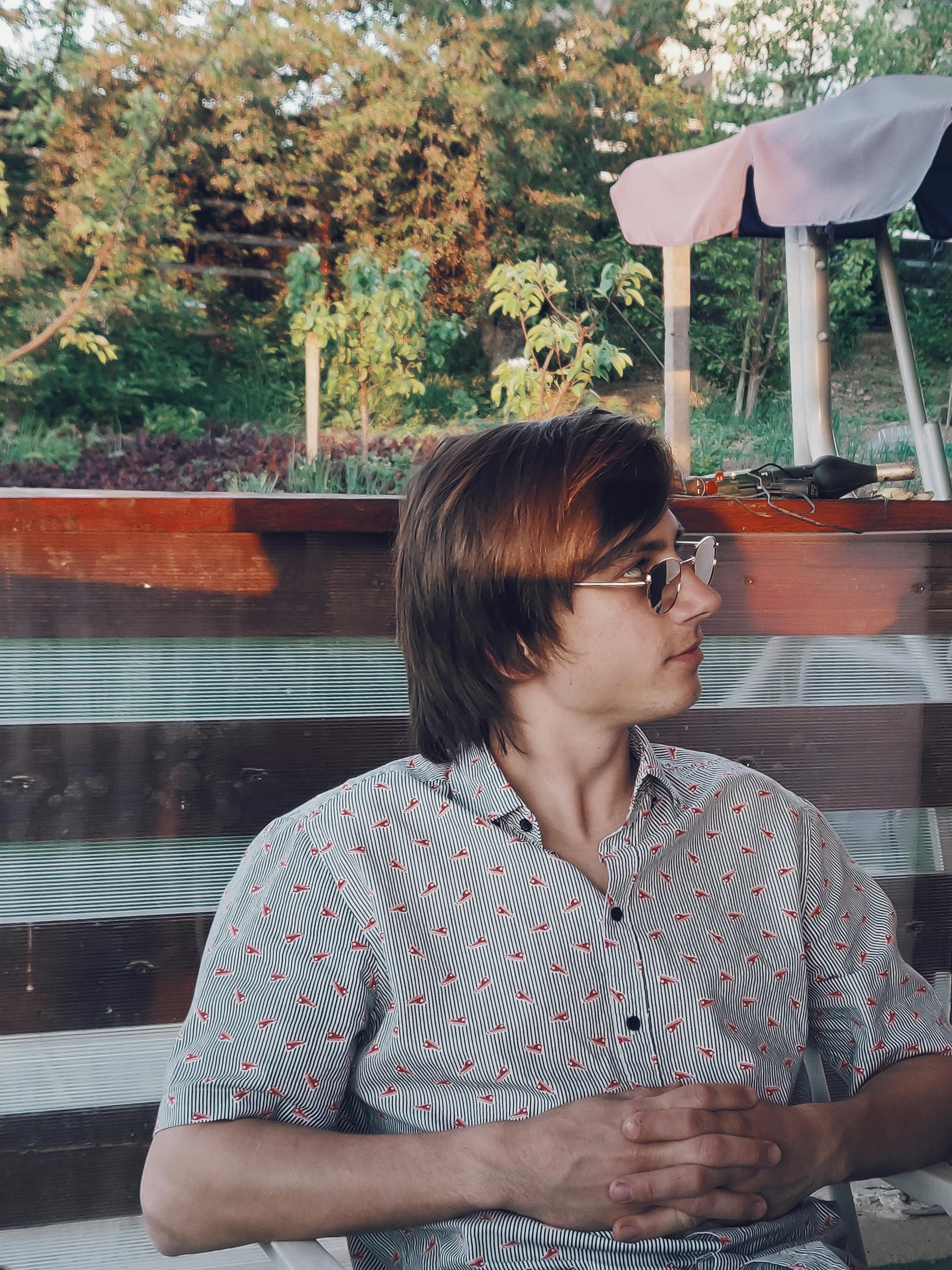 一个穿着时髦、身着图案衬衫的人，在户外享受阳光明媚的日子，侧面肖像显得随意自然