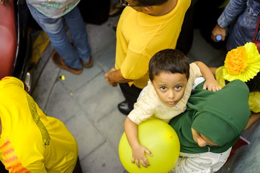 一个孩子拿着黄色气球，在繁忙的街道上抬头仰望，周围都是人