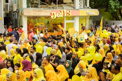 Free A large and colorful gathering of people participating in a vibrant street parade with yellow-themed attire and signs. Stock Photo