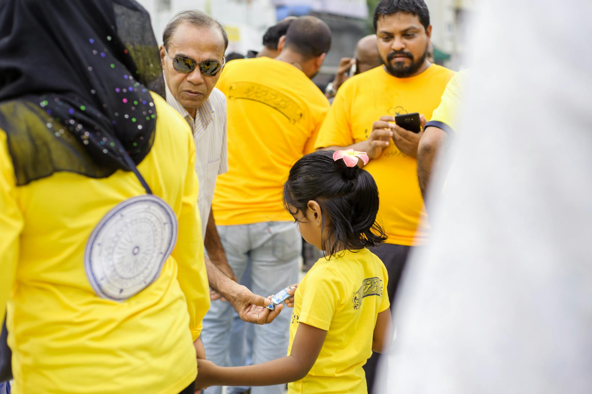 A diverse group of people in yellow shirts gather on a sunny street, engaging in a community event.