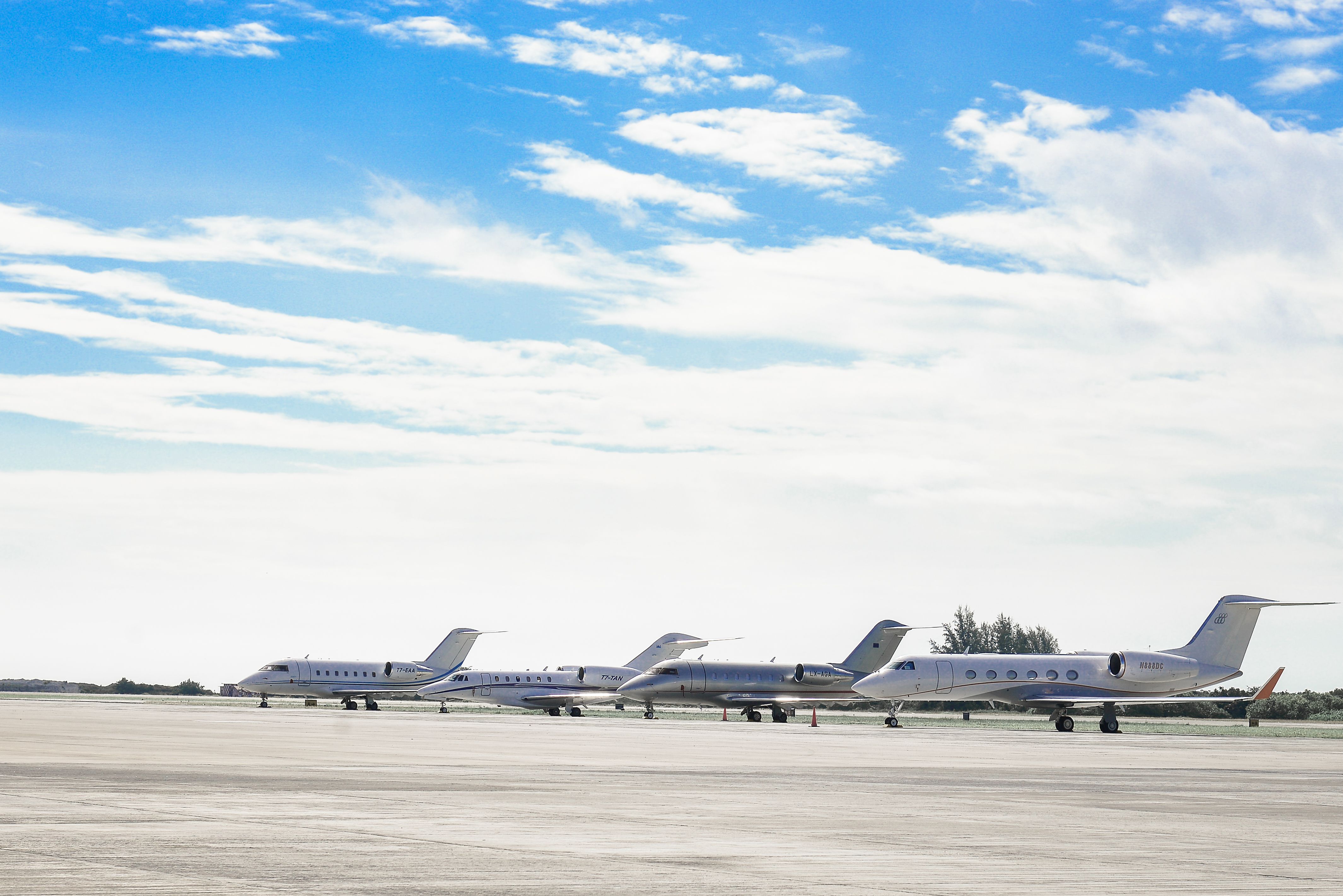 Four jets parked on an airport runway beneath a bright blue sky with scattered clouds
