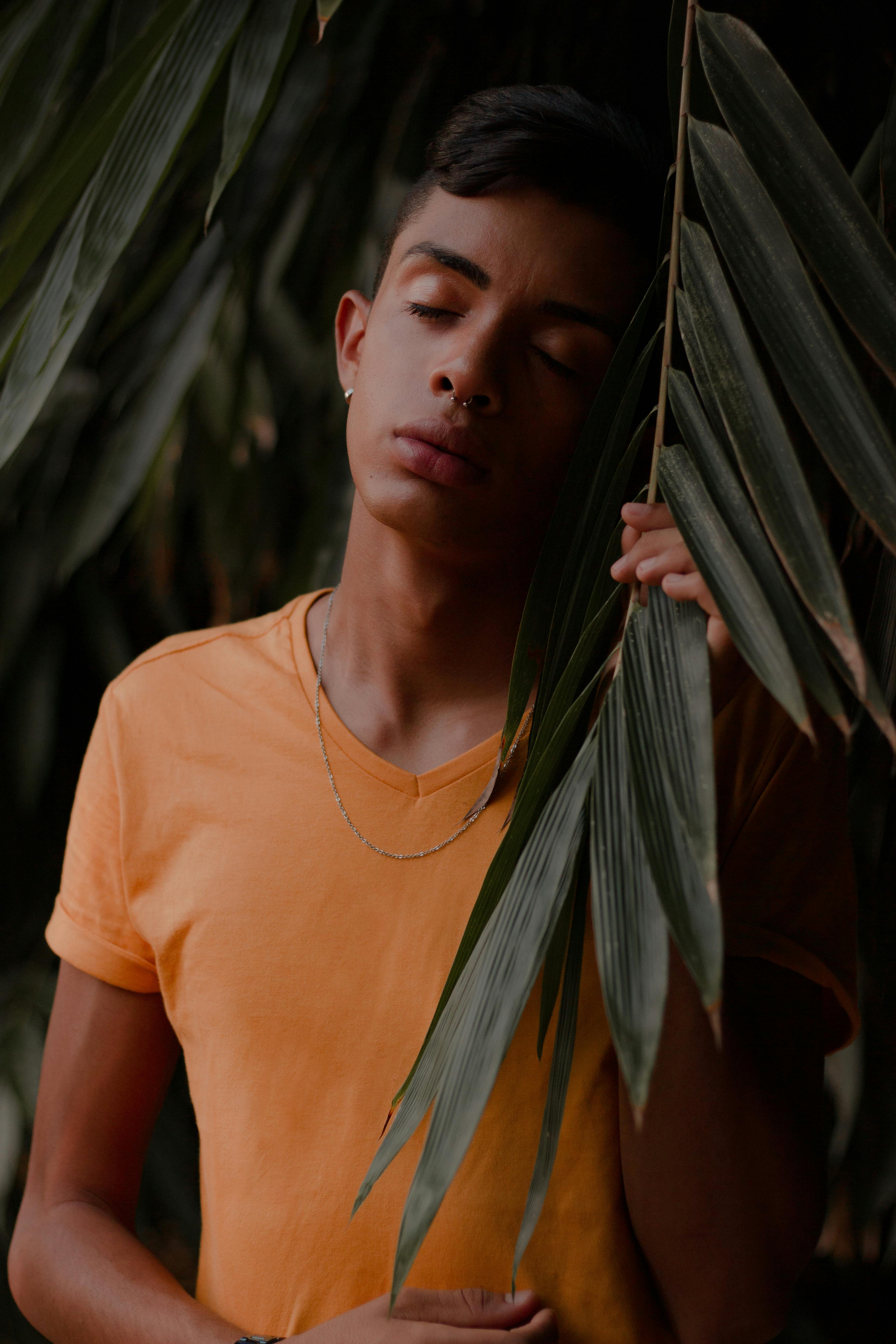 Photo Of Boy In Orange V Neck T Shirt Posing Next To Green Leafed
