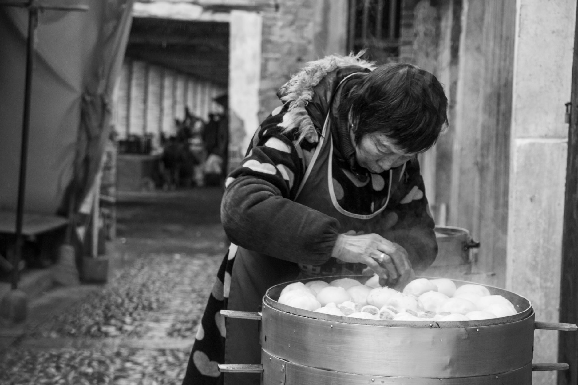 An elderly woman steams buns at a street market in Fuzhou, China. Captured in black and white.