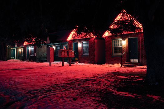 冬季夜晚，舒适的砖砌房屋外墙闪烁着红色霓虹灯，为雪地景观增添了光彩