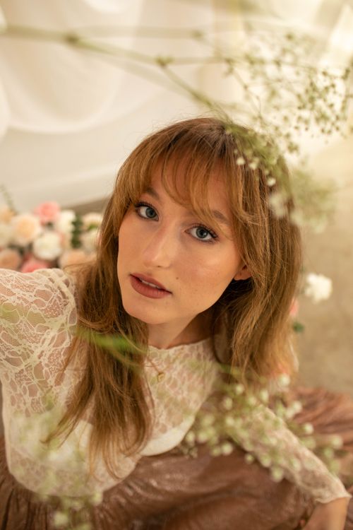 Free A portrait of a woman in a lace dress, surrounded by soft floral elements, exuding elegance. Stock Photo