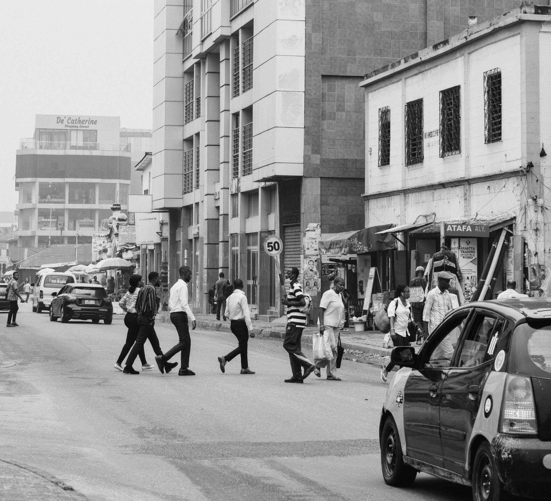 Black and white photo capturing pedestrians crossing a busy street in Accra, Ghana, showcasing city life.