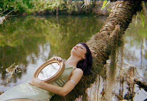 A woman laying on a tree branch holding a mirror