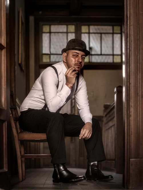 A man in a hat and suspenders sitting in a chair