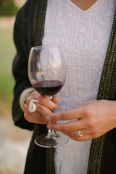Close-up of a woman in elegant attire holding a glass of red wine outdoors.