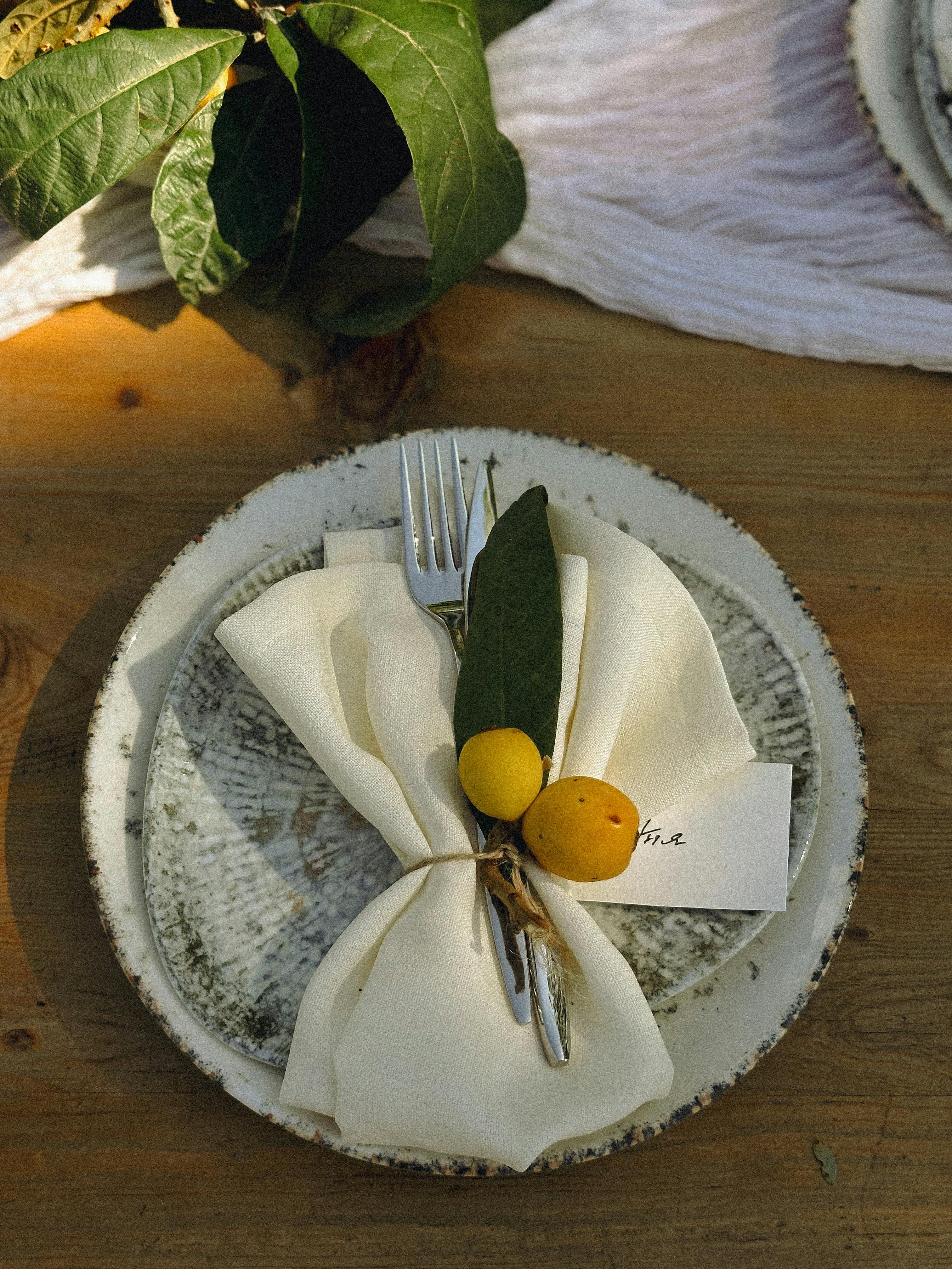 Elegant rustic table setting with fork, napkin, and citrus decoration on ceramic plate.