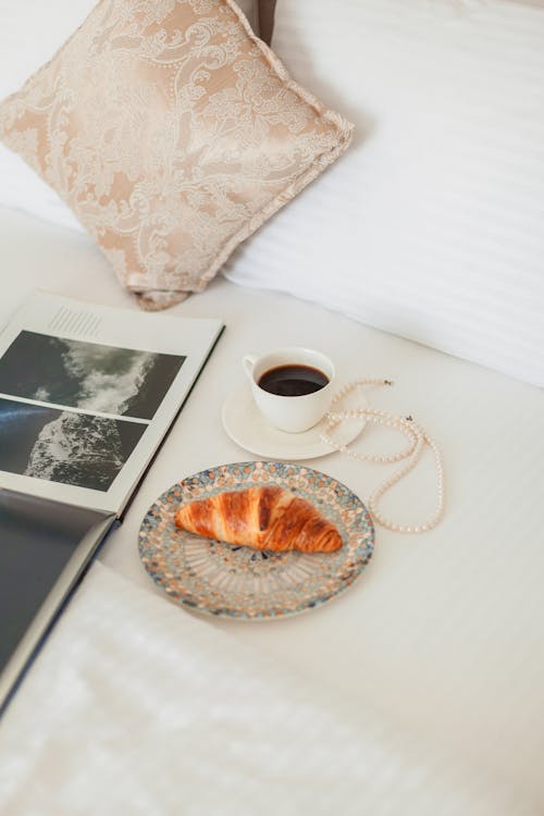 Free Croissant and Coffee near Pillow and Book Stock Photo