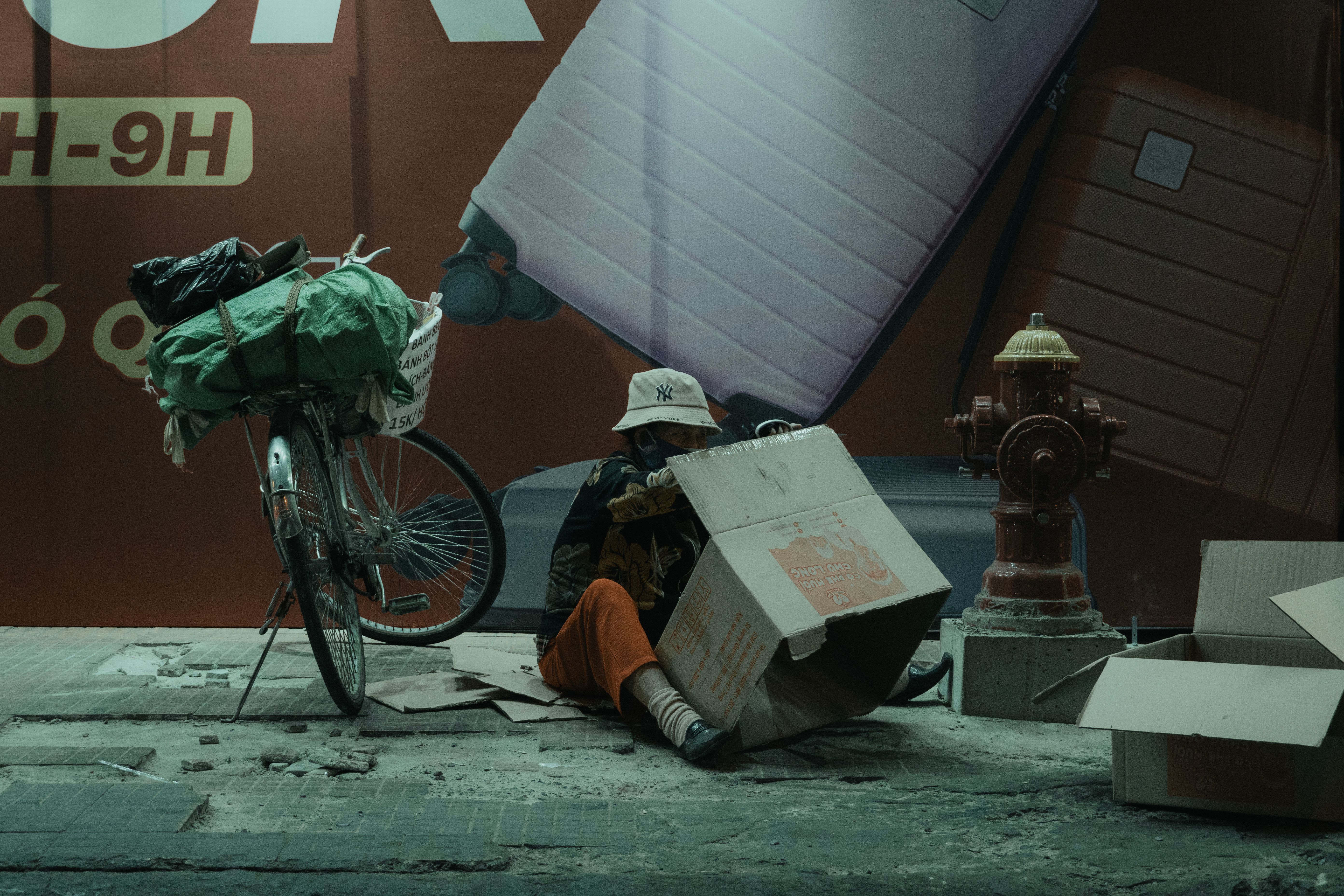 A man sitting by a bicycle with cardboard boxes in an urban setting at night.