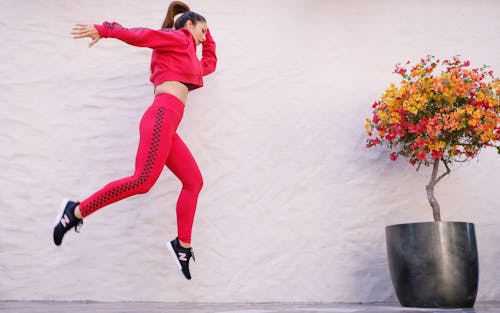 Free Woman in Red Tracksuit Jumping Near Wall Stock Photo