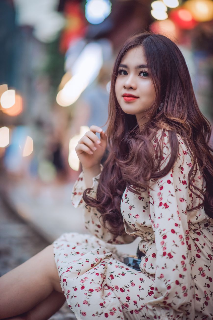 Portrait of an elegant woman sitting outdoors, surrounded by vibrant bokeh lights, exuding charm and grace.
