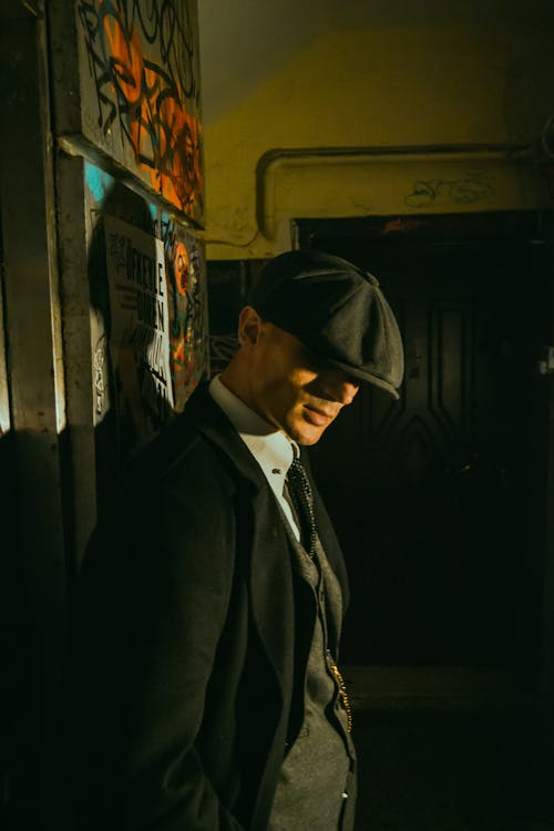 Free An elegant man in retro fashion wearing a hat and tie poses in an urban setting with graffiti. Stock Photo