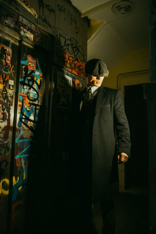 Free Mysterious man in a vintage coat and hat in a dimly lit alleyway with graffiti. Stock Photo