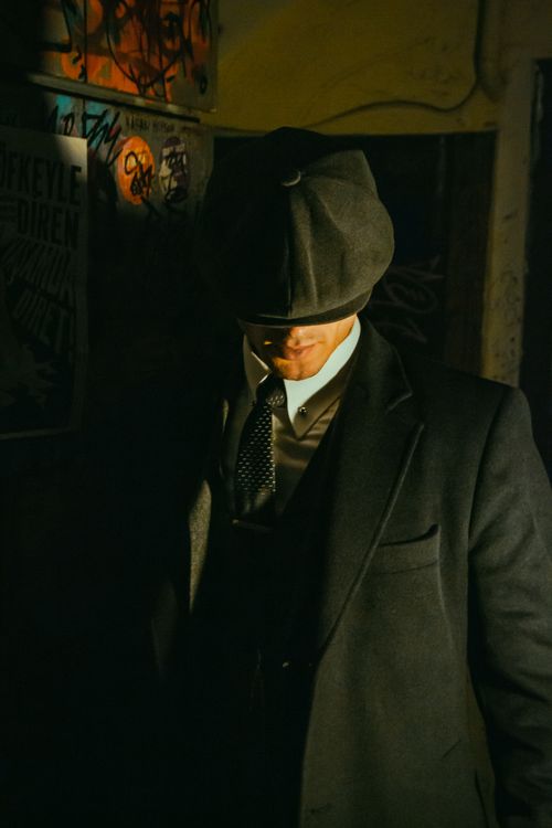 Free Stylish man in retro attire with hat, captured in a shadowy, artistic ambiance. Stock Photo