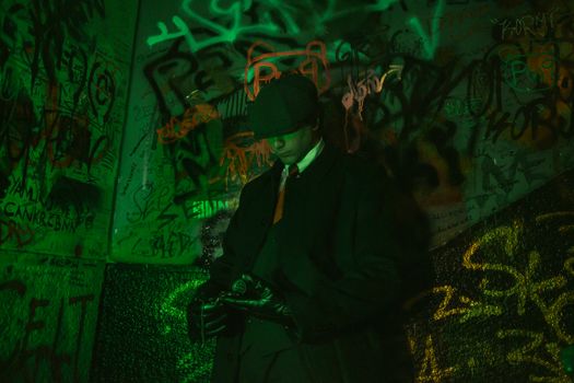 Stylish man in a trench coat and hat standing against vibrant graffiti wall, exuding retro elegance.