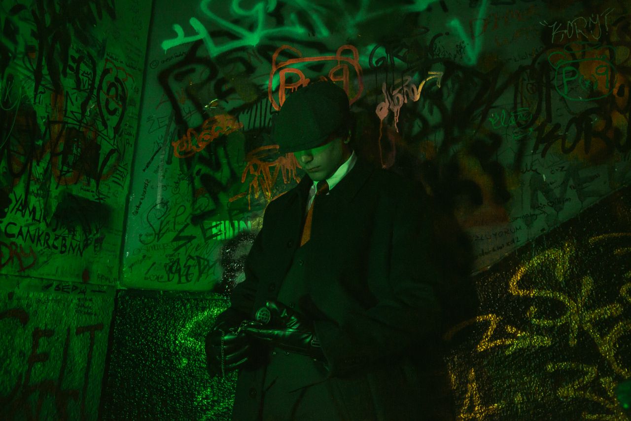stylish man in a trench coat and hat standing against vibrant graffiti