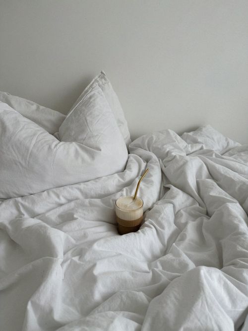 Free A cozy bedroom with a glass of coffee resting on white linen sheets, evoking relaxation. Stock Photo