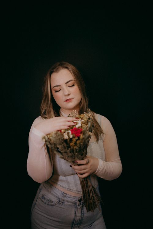 Free Portrait of a woman with closed eyes holding a bouquet, set against a dark studio backdrop. Stock Photo